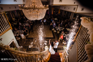 Bride and Groom walking down luxurious staircase for reception entrance at Mendenhall Inn. There is a crystal chandelier and sparklers