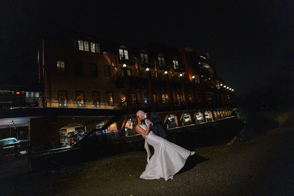groom dipping bride in front of River house at night time